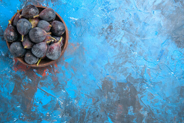 Top view of black mission figs in a small brown pot on the right side on blue background