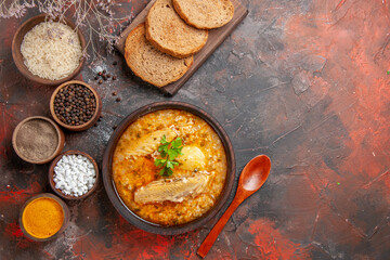 top view chicken soup wood spoon bowls with rice black pepper sea salt turmeric bread slices on cutting board on dark red background with copy space