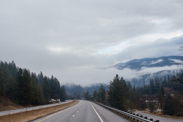 Highway with road signs on the sides among high mountains in the clouds in winter, along which trucks and cars travel. Idaho, USA, 12-5-2020