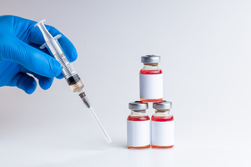 medical person holding syringe near vials with red liquid over gray background. blank label on vials. copy space. vaccination concept