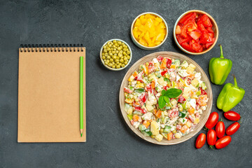 top close view of vegetable salad with different vegetables in bowls and notepad with pencil on side on grey table
