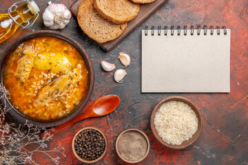 top view chicken soup bowls with pepper rice garlic wooden spoon oil bread slices on cutting board a notebook on dark red background