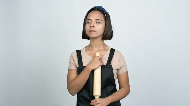 Young latin woman holding a rolling pin having doubts and questioning an idea over isolated background