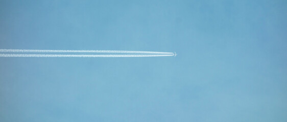 A flying plane in the sky leaves a white trail behind