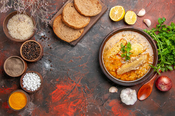 top view chicken soup garlic red onion spoon oil parsley lemon slices and bowls with rice black pepper sea salt turmeric bread slices on cutting board on dark red background
