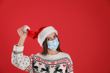 Fototapeta na wymiar Pretty woman in Santa hat and medical mask on red background, space for text