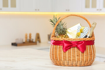 Fototapeta na wymiar Wicker basket full of gifts on wooden table in kitchen. Space for text
