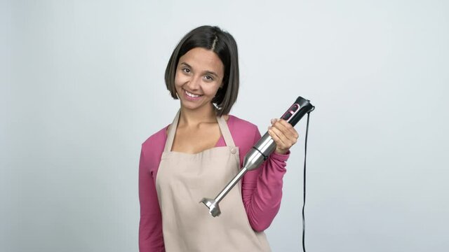 Young latin woman using hand blender with happy face over isolated background