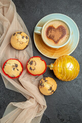 Above view of delicious freshly baked small cupcakes and a cup of frothy coffee on towel accessory on black background