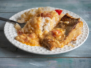 Fried fish with rice and sauce on a white plate with a fork on a wooden table