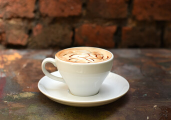 Flavored coffee in white cup on the wooden table. Background with red brick wall. 