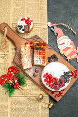 top view tart and waffles with berries on wood cutting board different xmas pendants a newspaper on dark background