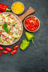 top view of veggie salad with cutleries and vegetables on side with free place for your text on right bottom on dark grey background