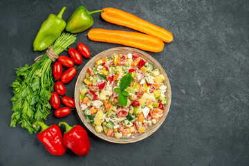 top close view of veggie salad with vegetables around it with free place for your text on dark grey background