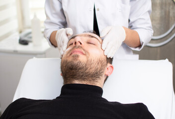 Portrait of handsome man getting face skin treatment. Close up of guy in beauty salon. Modern Cosmetology for men. Professional Cosmetologist. Men's Beauty Concept.