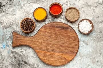 Top view of different spices necessary for cooking and wooden cutting board on ice background
