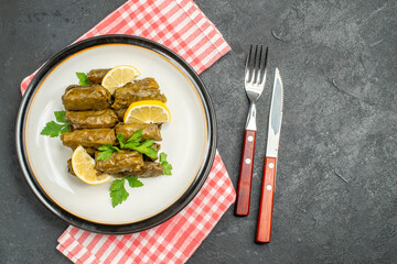 top view stuffed grape leaves on white plate knife and fork and napkin on dark background with copy space