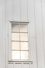 Closeup of exterior of white traditional barn with window reflecting the sky
