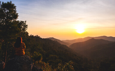 A female traveler sitting on the mountain peak and watching sunrise in the morning
