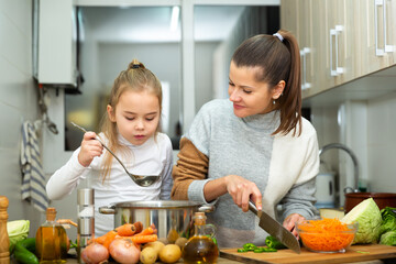 Happy little daughter and woman preparing vegetable soup together at home..