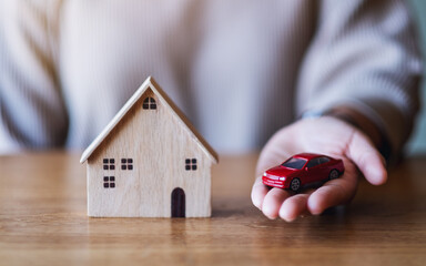 Closeup image of a woman holding and showing car figure model and wooden house model