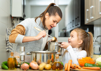 Positive young mother and little daughter tasting vegetable soup together