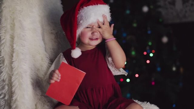 a child in red clothes is sitting waiting for the new year. the concept of celebrating Christmas at midnight. holiday costume. a girl writes a letter to Santa Claus. wish list