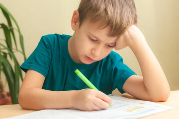 7 yeas old boy sitting at desk and doing homework. Child write notes in notebook, difficult homework, child concentrating on examples