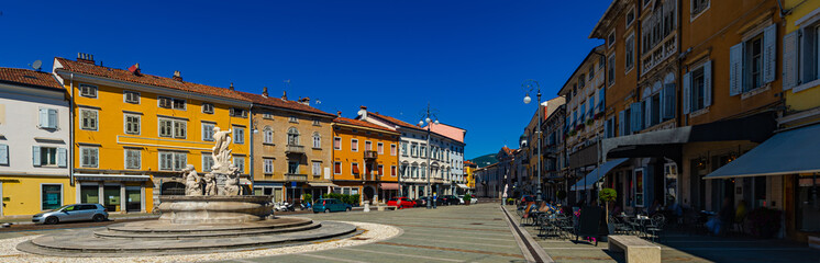 View of Victory Square (Piazza della Vittoria), central square of Gorizia with Neptune Fountain and colored buildings on sunny day, Italy
