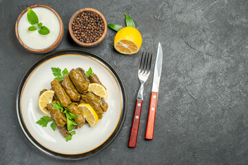 top view azerbaijani cuisine dolma on white oval plate bowls with natural yogurt black pepper a slice of lemon knife and fork on dark background with copy space