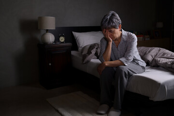 Depressed senior woman sitting in bed cannot sleep from insomnia