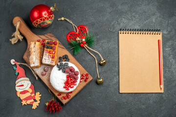 top view tart and waffles with berries on wood cutting board around different xmas pendants a notebook on dark background