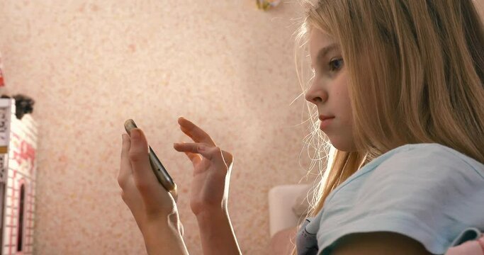 Little girl enjoys playing on smartphone phone in pink room art noise