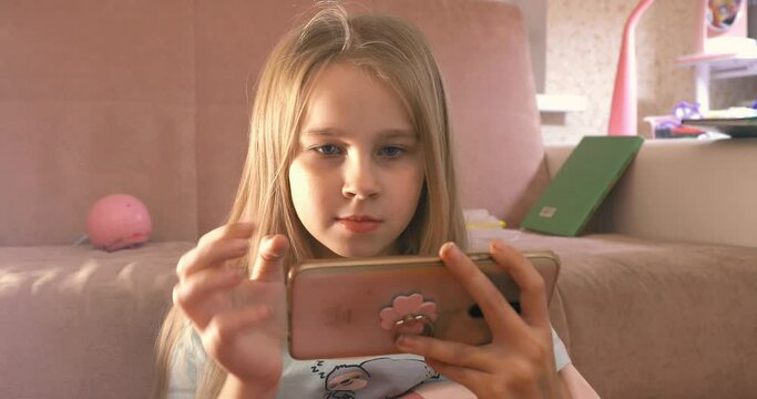 Little girl enjoys playing on smartphone phone in pink room art noise