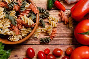 Terracotta bowl with tricolor fusilli noodles and cherry and round tomato, chili peppers, garlic and parsley. Food raw material concept. Chopped angle.