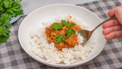 Delicious sour cream chicken paprika served with rice and fresh parsley close up on a plate on kitchen table