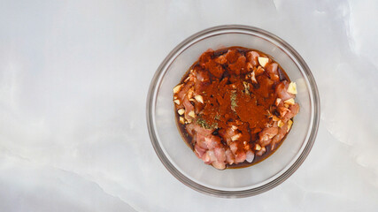 Chopped chicken fillet marinated with garlic, seasoning, paprika, and soy sauce close up in a glass bowl on marble background