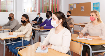 Portrait of positive woman sitting in class working during group business training, all people wearing face masks for disease protection
