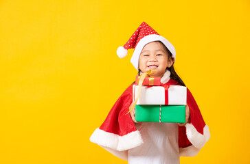 Asian little cute girl smile and excited, Kid dressed in red Santa Claus hat hold gift box on hands concept of holiday Christmas Xmas day or Happy new year, studio shot isolated on yellow background