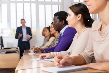 Side view of student group working on lecture in classroom, making notes. High quality photo