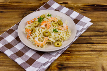 Spaghetti pasta with prawns, green olives and parsley on wooden table