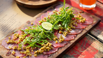 Italian dish fresh tuna carpaccio on wooden table. Outdoor sun light. Luxurious cuisine background.