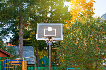 Basket with a net for playing basketball on a Board in the courtyard of a residential building in the city.Trees in autumn with yellow foliage are illuminated by the sun. The theme of a healthy lifest