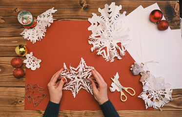 Female Hands making white paper snowflakes over wooden table