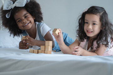 Two little kid girls, African and Asian children enjoy playing build wooden block toys together on...