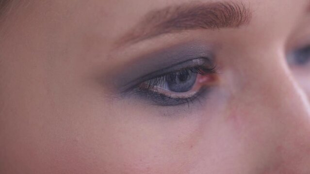 The gray eye of a young woman painted with gray shadows.