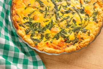 Seafood, salmon fish and baby spinach leaves quiche pie - homemade recipe pie on wooden table background with copy space, selective focus
