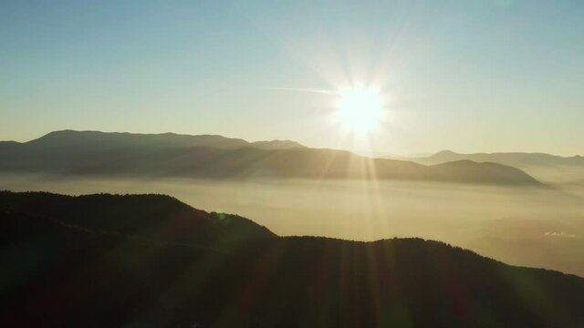 
Aerial view of sunrise, sunset in the mountains. The sun with rays illuminates the mountain ranges and peaks which are covered with smoke and clouds. Beautiful background landscape video.