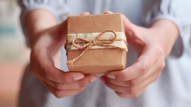 Young woman hands holding gift box for birthday or christmas. 	gives it by hands to camera.