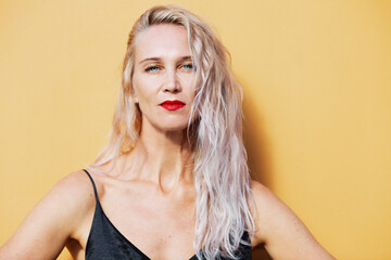 Serious young blonde woman in sunlight on the background of a yellow wall of a building. Close-up.